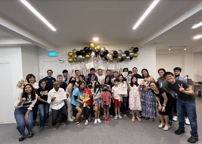 A group of people posing indoors with certificates and balloons in a festive setting.